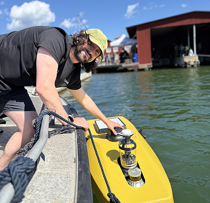 SMaRC researcher leaning over a underwater robot lying in the water.